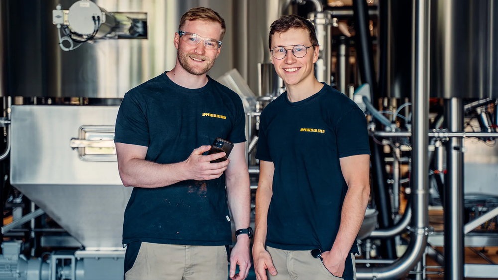 Zwei Mitarbeiter der Firma Appenzeller Bier lächeln in die Kamera; einer der Männer hält ein Smartphone in den Händen, aufgenommen 2023